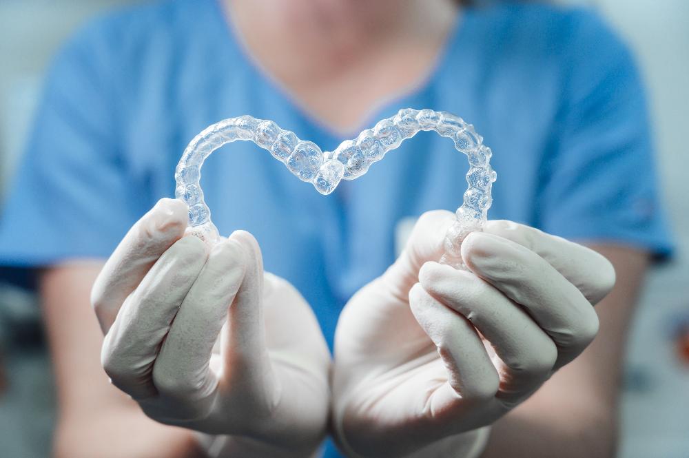 A dentist holding Invisalign trays in the shape of a heart