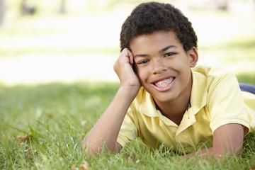 A smiling boy with braces laying in the grass