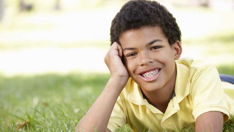 A smiling boy with braces in the grass