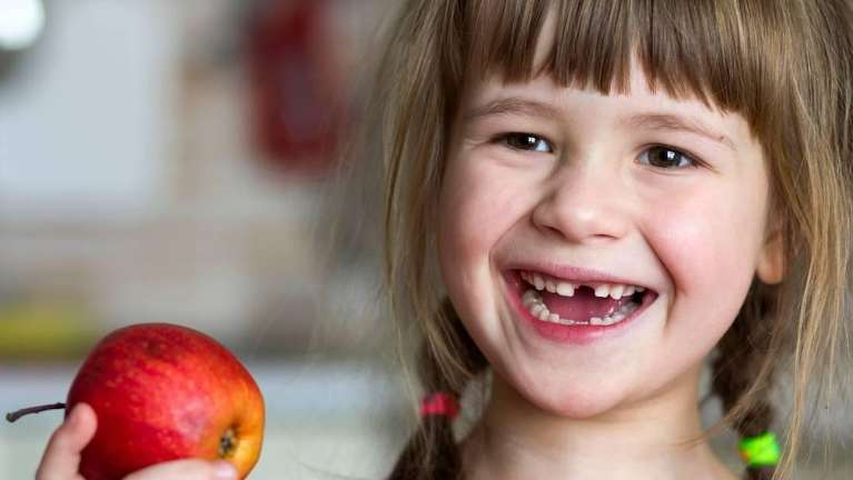 A smiling child with a missing tooth holding an apple