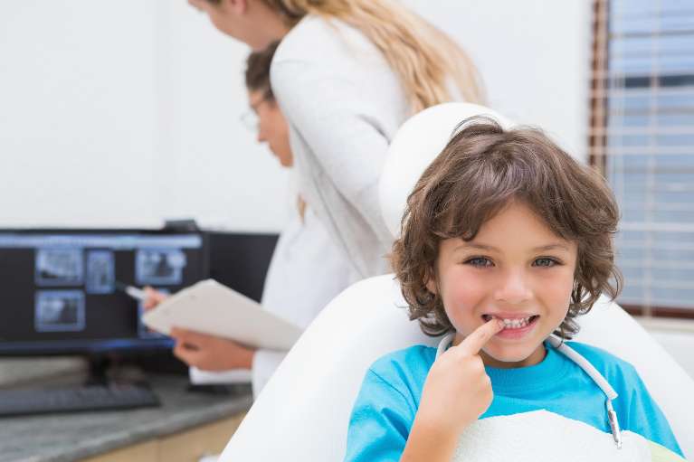 A child showing his teeth while the dentists look at his xrays