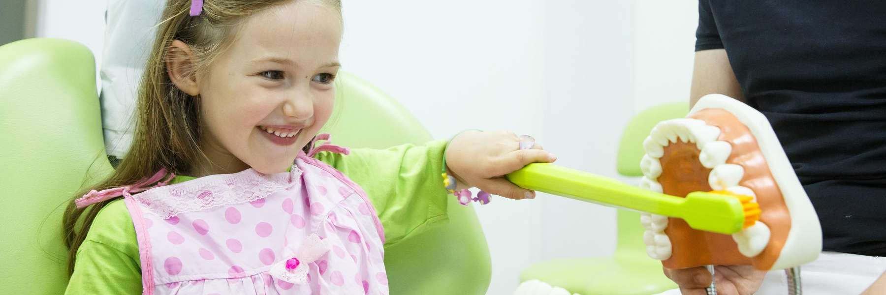 A smiling girl brushes a tooth model at her Corona pediatric dentist